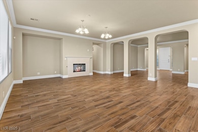 Unfurnished living room featuring ornamental molding, a fireplace, arched walkways, wood finished floors, and a chandelier