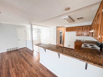 Kitchen with electric stove, brown cabinets, a peninsula, a textured ceiling, and dark wood-style floors