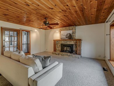 Carpeted living area with a ceiling fan, a stone fireplace, and wooden ceiling