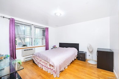 Bedroom with a baseboard heating unit, light wood finished floors, and a wall mounted air conditioner