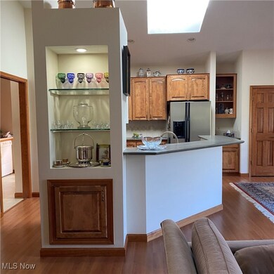 Kitchen with open shelves, dark wood-style flooring, stainless steel fridge, and brown cabinetry