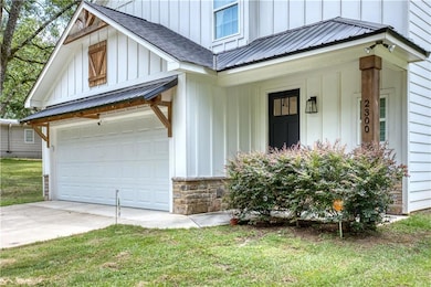 View of front facade with board and batten siding, a garage, a metal roof, and driveway