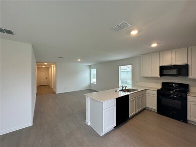 Kitchen with light wood finished floors, a sink, black appliances, visible vents, and a peninsula