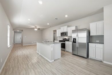 Kitchen featuring stainless steel appliances, white cabinets, a ceiling fan, a kitchen island with sink, and recessed lighting