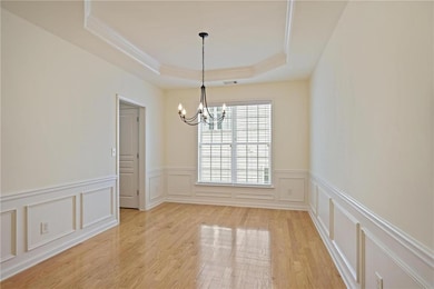 Empty room featuring a chandelier, a tray ceiling, a decorative wall, crown molding, and light wood finished floors