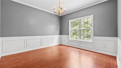 Spare room featuring a chandelier, ornamental molding, wood finished floors, wainscoting, and a decorative wall