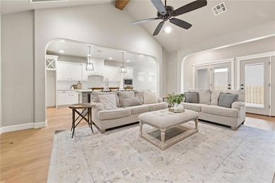 Living area featuring arched walkways, light wood-style flooring, beam ceiling, high vaulted ceiling, and a ceiling fan