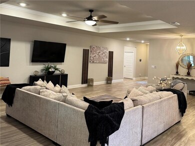 Living room with crown molding, a tray ceiling, wood finished floors, a ceiling fan, and recessed lighting