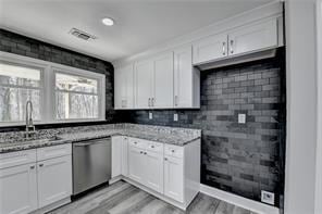 Kitchen with stainless steel dishwasher, light wood-type flooring, and white cabinetry
