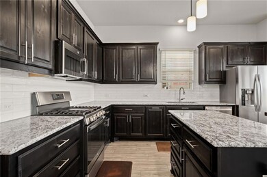 Kitchen with stainless steel appliances, hanging light fixtures, tasteful backsplash, light stone countertops, and dark brown cabinetry