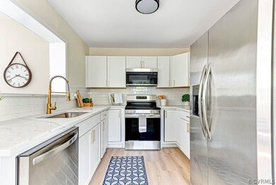 Kitchen with light stone counters, light hardwood / wood-style floors, stainless steel appliances, tasteful backsplash, and white cabinets