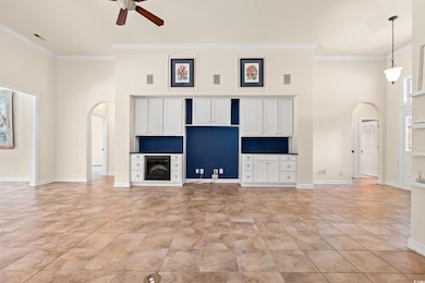 Unfurnished living room featuring arched walkways, a towering ceiling, ornamental molding, and ceiling fan