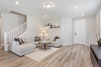 Living room with stairs, light wood finished floors, and recessed lighting