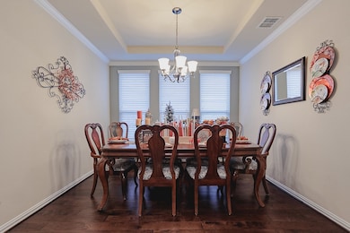 Dining room featuring crown molding, dark wood-type flooring, a chandelier, and a tray ceiling