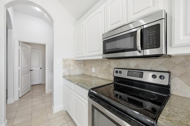 Kitchen with appliances with stainless steel finishes, light stone counters, white cabinetry, decorative backsplash, and lofted ceiling