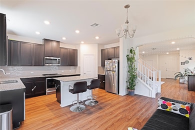 Kitchen with a kitchen bar, appliances with stainless steel finishes, dark brown cabinetry, light wood finished floors, and light stone countertops