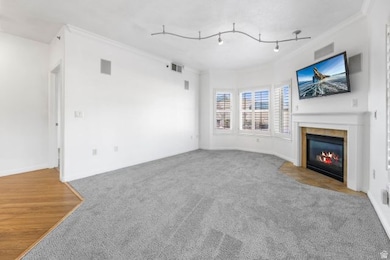Unfurnished living room with ornamental molding, carpet, a fireplace with flush hearth, and wood finished floors