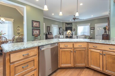 Kitchen featuring dishwasher, brown cabinetry, light stone countertops, decorative light fixtures, and open floor plan