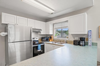 Kitchen with white cabinets, under cabinet range hood, a sink, and appliances with stainless steel finishes