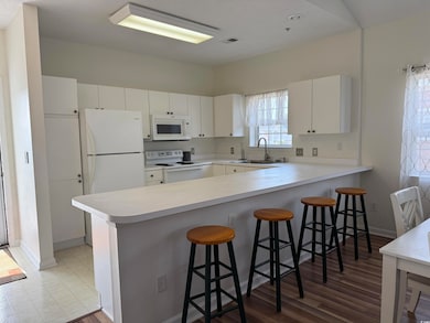 Kitchen with white appliances, a sink, a peninsula, baseboards, and light countertops