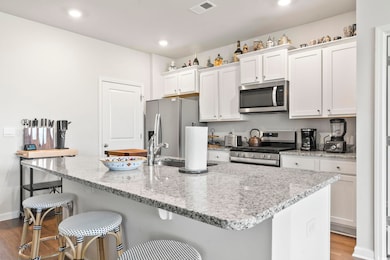 Kitchen with appliances with stainless steel finishes, dark wood finished floors, white cabinetry, a kitchen breakfast bar, and an island with sink