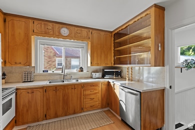 Kitchen with stainless steel appliances, light countertops, brown cabinets, light wood-style flooring, and a wainscoted wall