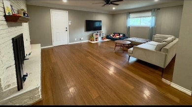 Living area featuring crown molding, dark wood finished floors, a brick fireplace, and ceiling fan