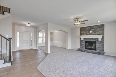 Entrance foyer featuring a ceiling fan, arched walkways, stairs, light wood-type flooring, and a stone fireplace