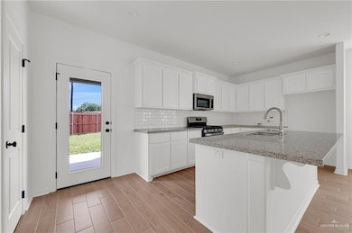 Kitchen featuring stainless steel appliances, light wood-style floors, backsplash, and light stone counters