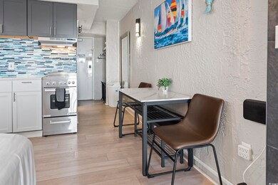 Kitchen with a textured wall, under cabinet range hood, stainless steel electric range, light wood-style floors, and backsplash