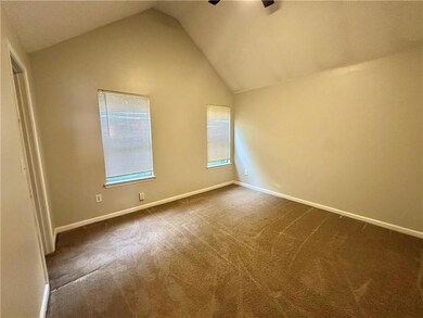 Spare room featuring vaulted ceiling, a ceiling fan, dark colored carpet, and baseboards