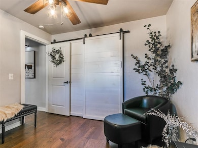 Living area featuring a barn door, dark wood-type flooring, and ceiling fan