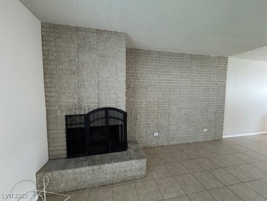 Unfurnished living room with tile patterned floors, a textured ceiling, and a brick fireplace