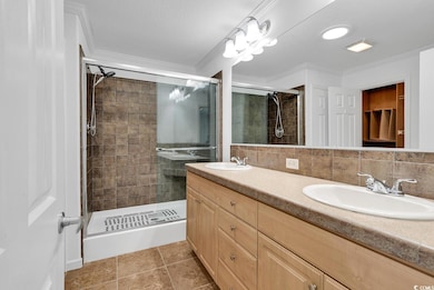 Bathroom featuring a stall shower, ornamental molding, double vanity, tile patterned floors, and tasteful backsplash