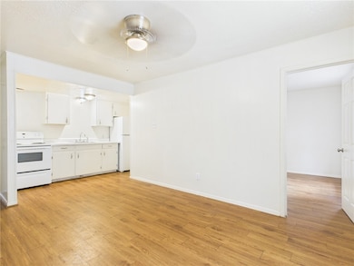 Kitchen with white appliances, light countertops, light wood-type flooring, white cabinets, and ceiling fan
