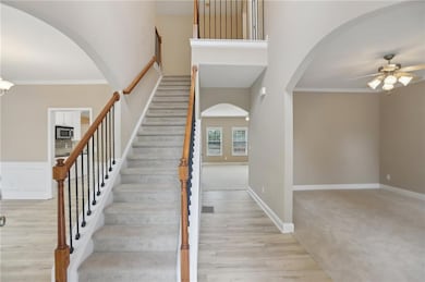 Stairway with a ceiling fan, arched walkways, wood finished floors, crown molding, and a high ceiling