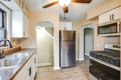 Kitchen with light hardwood / wood-style floors, appliances with stainless steel finishes, ceiling fan, backsplash, and white cabinetry