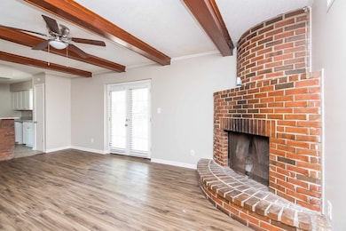 Unfurnished living room with beamed ceiling, wood finished floors, a fireplace, baseboards, and ceiling fan