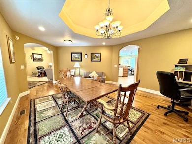 Dining area featuring arched walkways, a chandelier, a tray ceiling, and recessed lighting