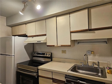 Kitchen featuring electric stove, light countertops, under cabinet range hood, and cream cabinets