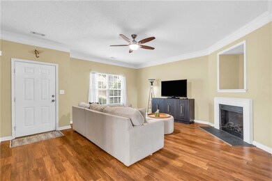 Living room with ceiling fan, wood finished floors, ornamental molding, and a fireplace with flush hearth