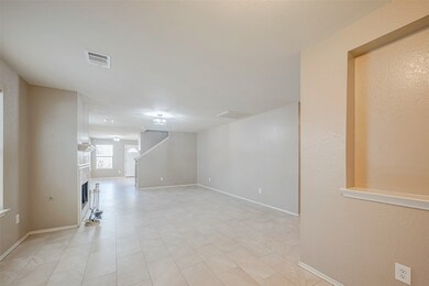 Open-plan living area with neutral-color walls and tile flooring. It features a fireplace on the left and a staircase leading to the upper floor.