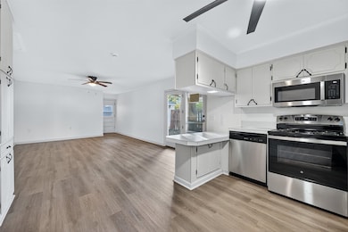 Kitchen featuring ceiling fan, stainless steel appliances, light countertops, open floor plan, and light wood-type flooring