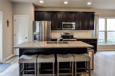 Kitchen featuring appliances with stainless steel finishes, decorative backsplash, light stone counters, a breakfast bar, and recessed lighting