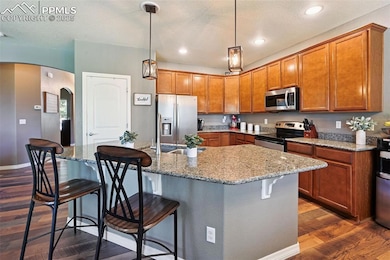 Kitchen with arched walkways, dark wood-style flooring, brown cabinetry, appliances with stainless steel finishes, and a breakfast bar area