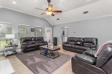 Living room with light wood-type flooring, ceiling fan with notable chandelier, lofted ceiling, and ornamental molding