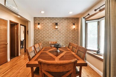 Large dining room with distinctive accent wall, bay window, attractive lighting and wood floor opens to entry foyer, living room and kitchen (across foyer)