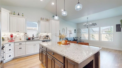 Kitchen featuring light wood finished floors, light stone countertops, vaulted ceiling, pendant lighting, and white cabinetry