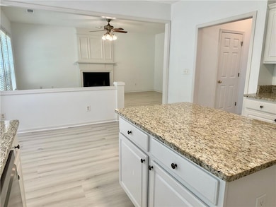Kitchen with ceiling fan, light wood-type flooring, light stone countertops, white cabinetry, and a center island