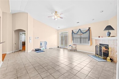 Unfurnished living room featuring a ceiling fan, arched walkways, lofted ceiling, light tile patterned floors, and a tiled fireplace